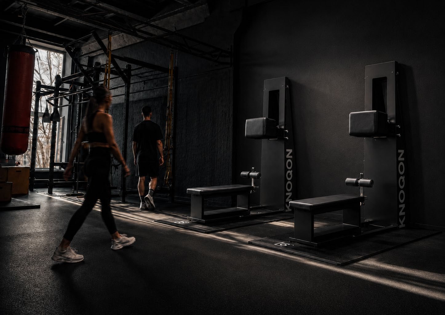 Two people walking towards two KNOQON machines in dramatic side light